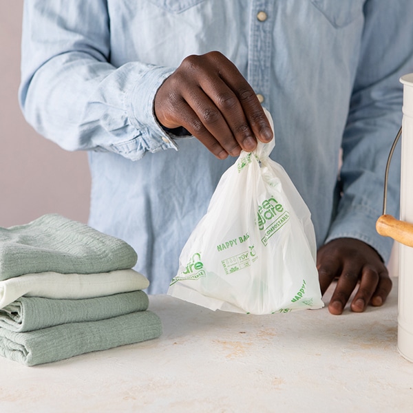 Person holding Green Aware compostable nappy bag beside stack of muslin cloths